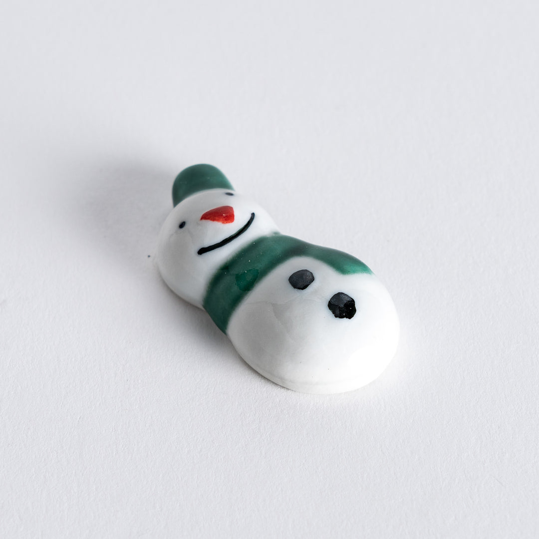 Diagonal angle view of snowman chopstick rest with a green hat and scarf, emphasizing the cheerful and detailed design.