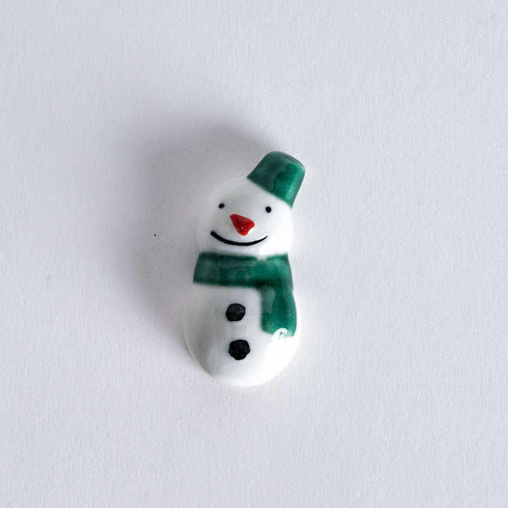 Snowman chopstick rest featuring a green hat and scarf, designed to hold chopsticks in a playful and festive way.