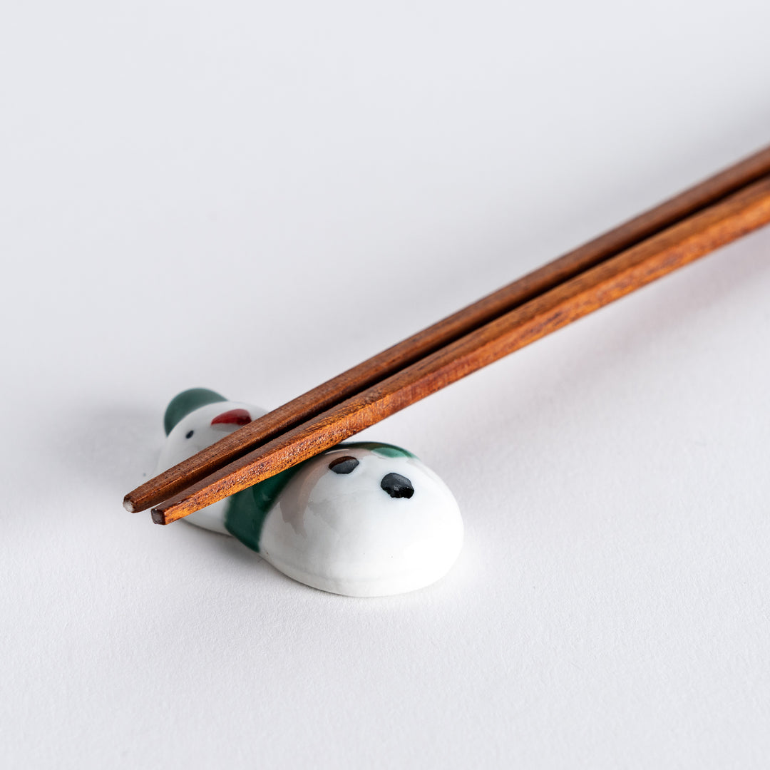 Close-up of snowman chopstick rest with chopsticks placed on it, highlighting the green hat and scarf design.