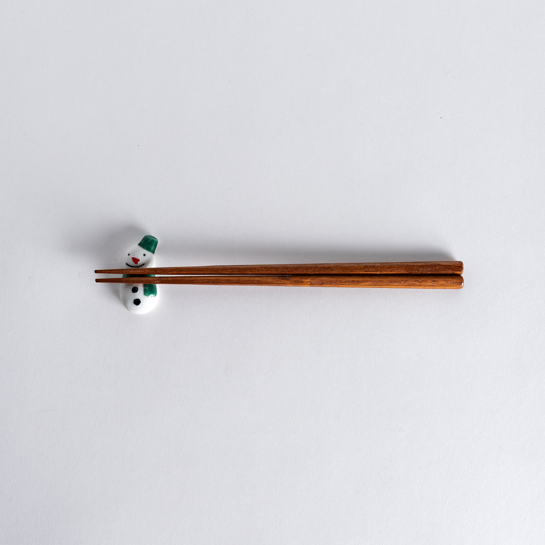 Full view of snowman chopstick rest with chopsticks resting on it, showcasing the charming snowman design with a green hat and scarf.