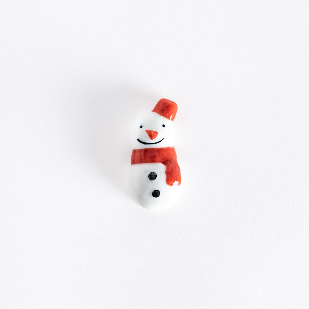 A red-scarfed ceramic snowman chopstick rest with a cheerful smile and matching red hat.