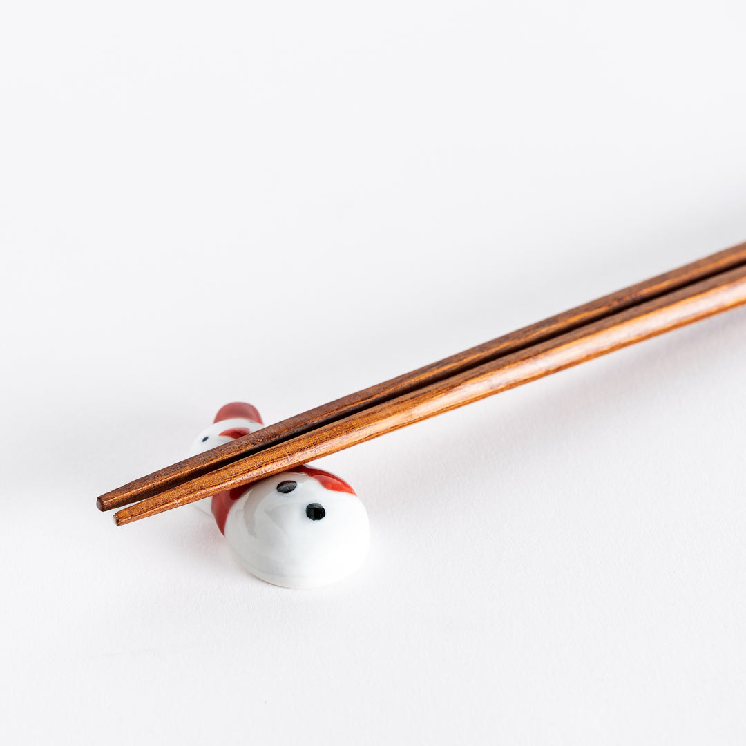 A close-up of the red-scarfed snowman chopstick rest with chopsticks resting on it, highlighting its vibrant details.