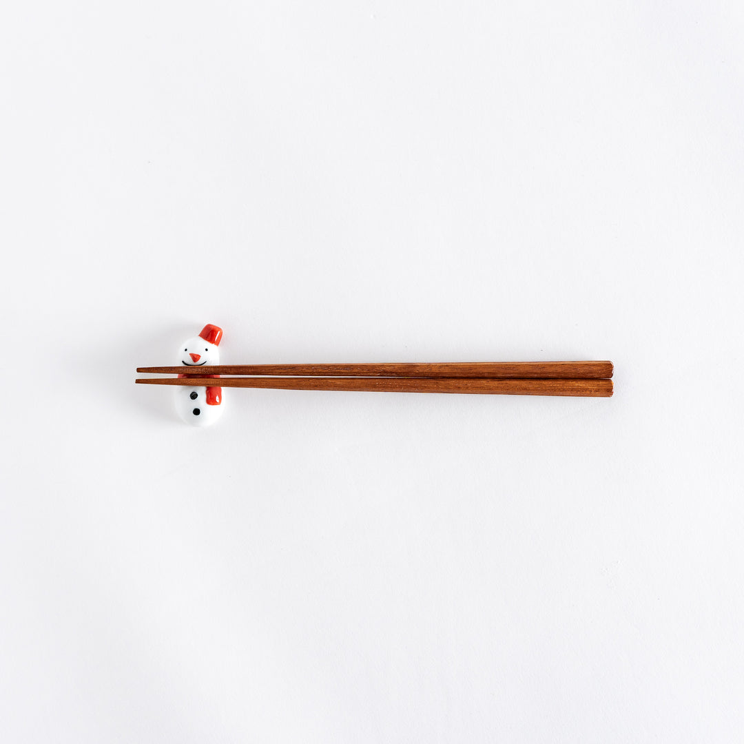 A wide view of the red-scarfed snowman chopstick rest with chopsticks placed on it, showcasing its playful design.