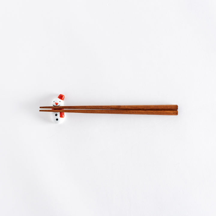 A wide view of the red-scarfed snowman chopstick rest with chopsticks placed on it, showcasing its playful design.