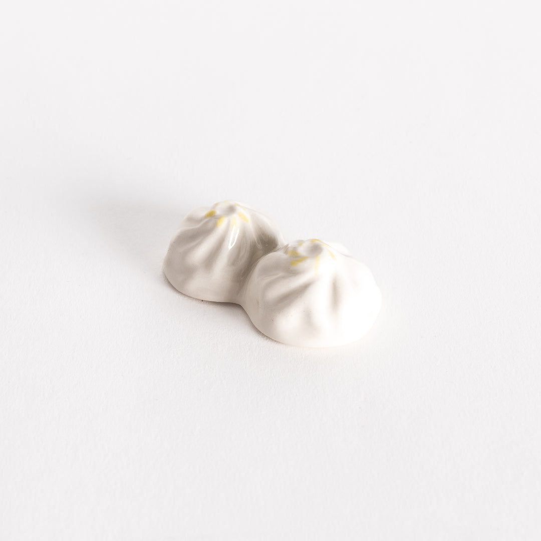 Top-down view of a white soup dumpling-shaped chopstick rest with detailed folds and a hint of yellow accent.