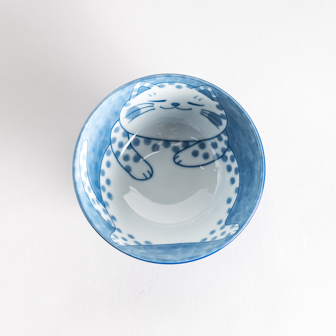 A rice bowl featuring a chubby blue-spotted white cat, sitting contentedly.