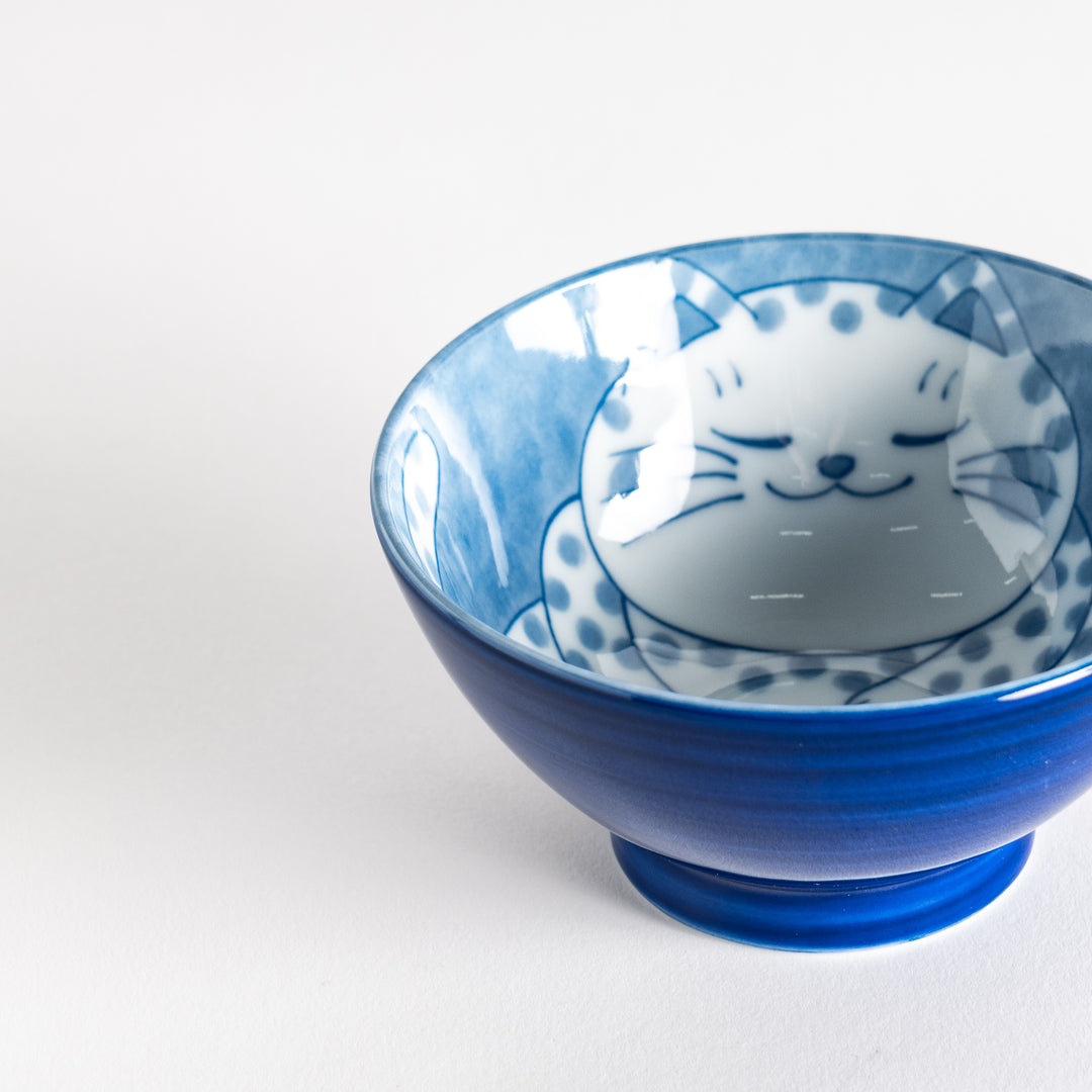 A rice bowl featuring a chubby blue-spotted white cat, sitting contentedly.