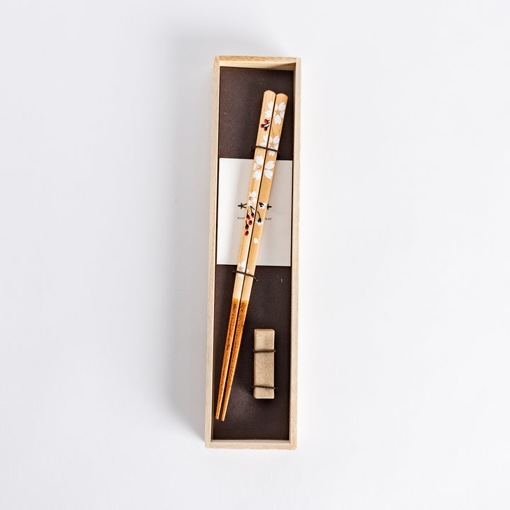 Elegant floral design on chopsticks featuring soft white flowers, placed in a light wood box with a traditional touch.