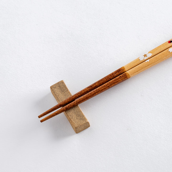 Close-up view of cherry blossom-patterned chopsticks with red and white floral accents, with a simple beige chopstick rest.