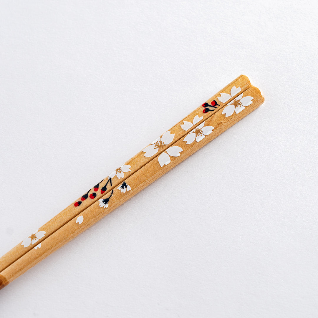 Close-up of cherry blossom-patterned chopsticks with a delicate white flower design, resting on a beige chopstick holder.