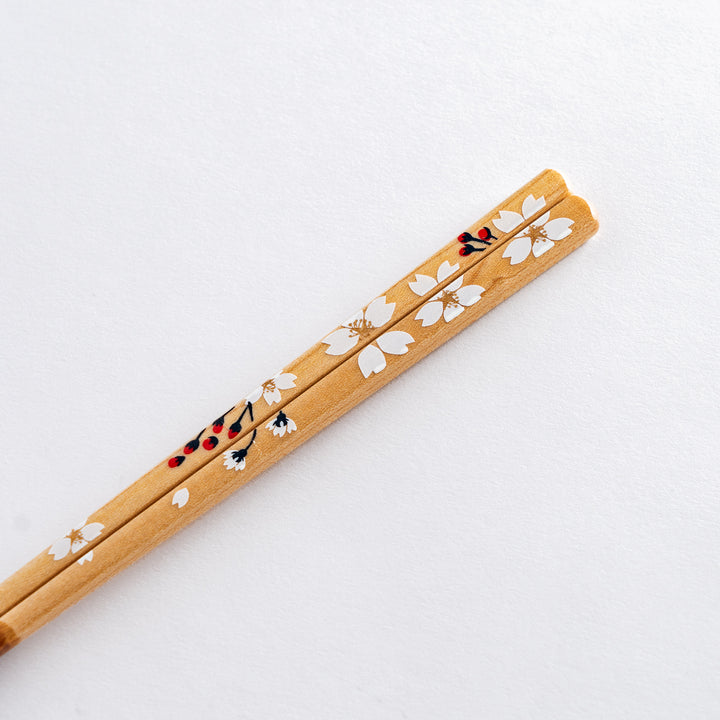 Close-up of cherry blossom-patterned chopsticks with a delicate white flower design, resting on a beige chopstick holder.