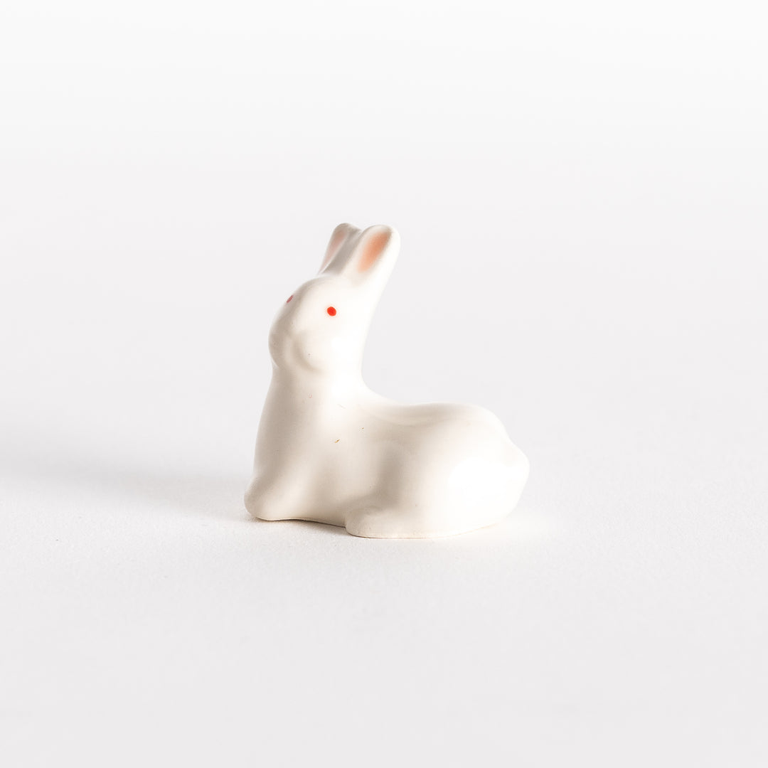 A slightly angled view of the ceramic rabbit chopstick rest, emphasizing its sitting posture, red eyes, and soft pink ear details.