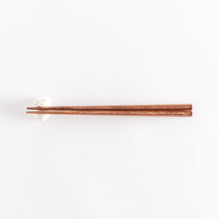 A wide view of the ceramic rabbit chopstick rest with chopsticks resting on it, showcasing its elegant and playful design.