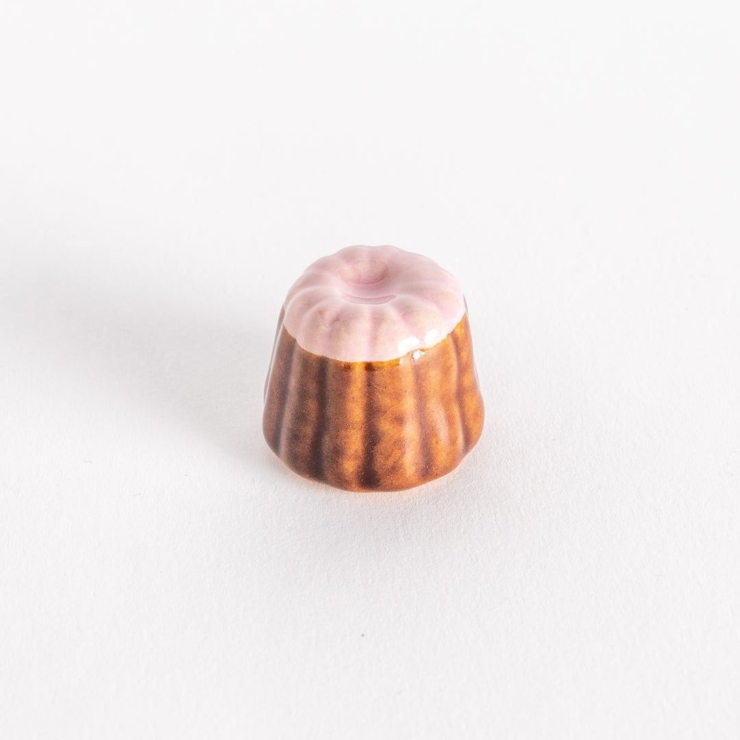 A ceramic chopstick rest shaped like a strawberry canelé, featuring a glossy pink top and ridged brown sides on a white background.