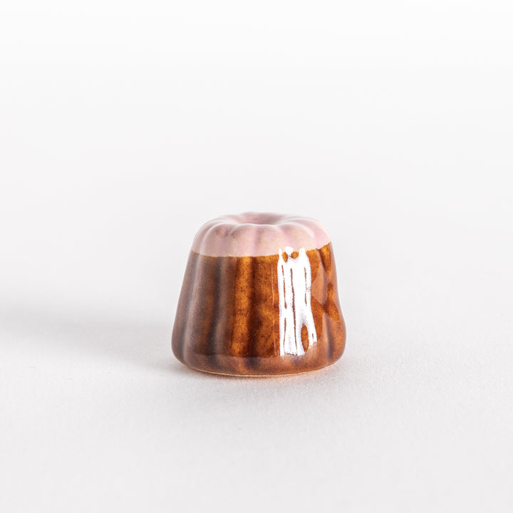 A front-facing view of the ceramic strawberry canelé chopstick rest, showcasing its ridged brown sides and smooth pink top.