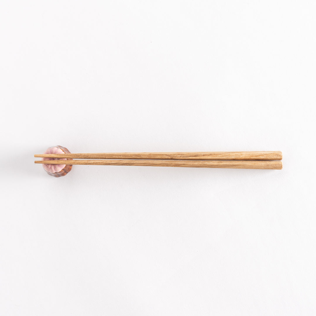 A wide view of the strawberry canelé chopstick rest with chopsticks placed on it, emphasizing its elegant design and unique color contrast.