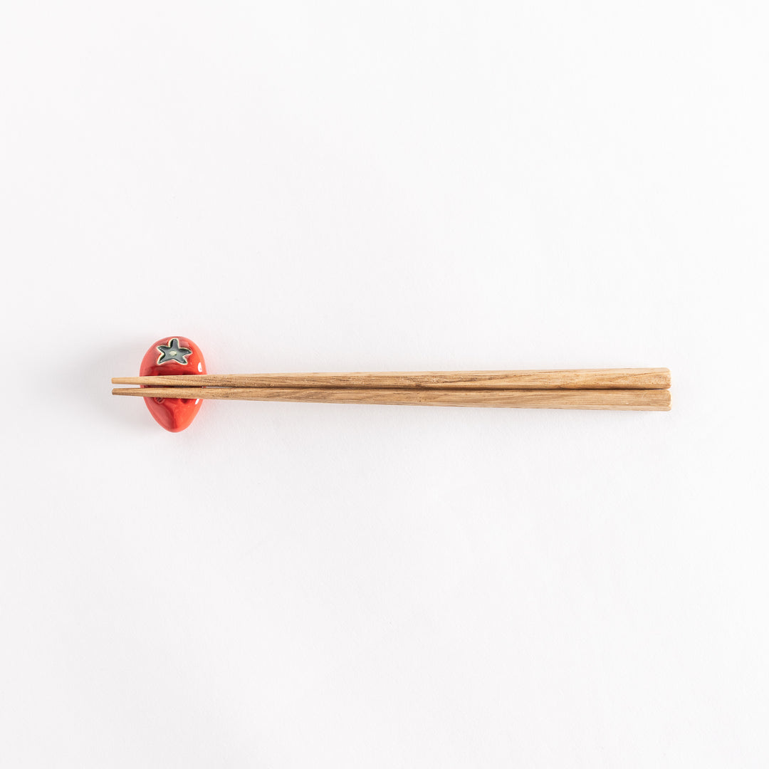 The strawberry chopsticks rest with chopsticks resting across, showcasing its realistic strawberry design.