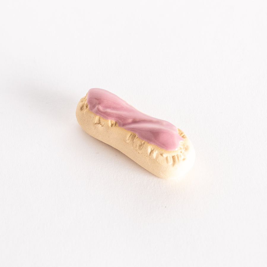 A ceramic chopsticks rest shaped like a strawberry éclair with pink glaze and golden biscuit details.