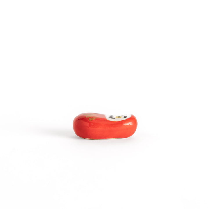 A side view of the red daruma chopstick rest, showcasing its rounded shape and smooth, glossy finish.