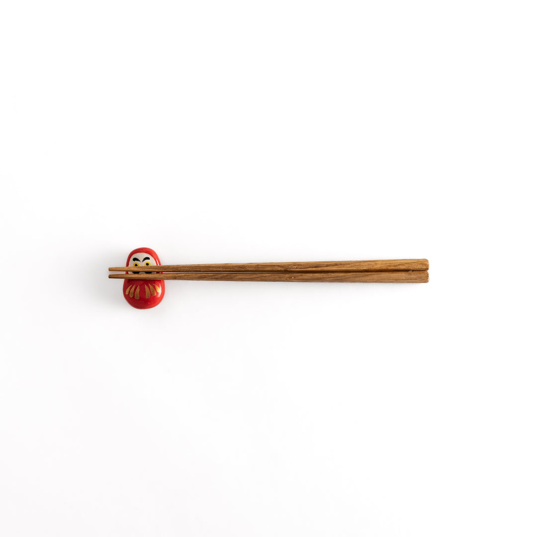 A distant view of chopsticks placed on the daruma-shaped chopstick rest, showcasing its overall design and color contrast.