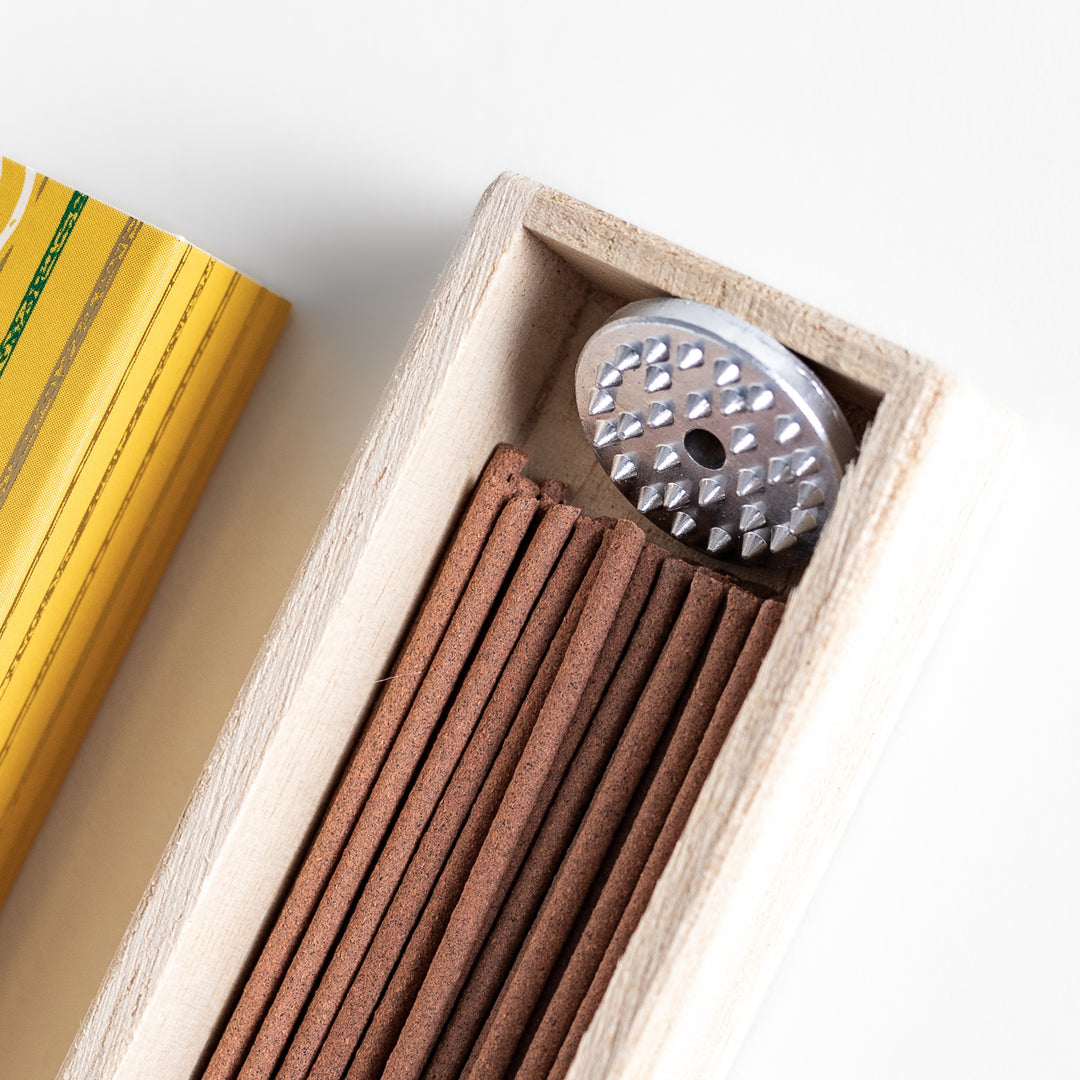 Incense in a light wooden box with warm brown sticks, elegantly packaged in a vibrant yellow design featuring white circular patterns for a refreshing and uplifting ambiance.