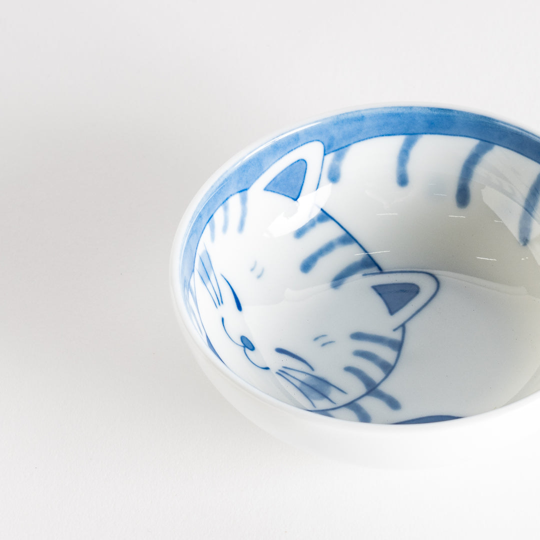 A dessert bowl with a blue-striped cat, smiling contentedly.