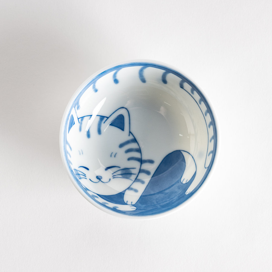 A dessert bowl with a blue-striped cat, smiling contentedly.