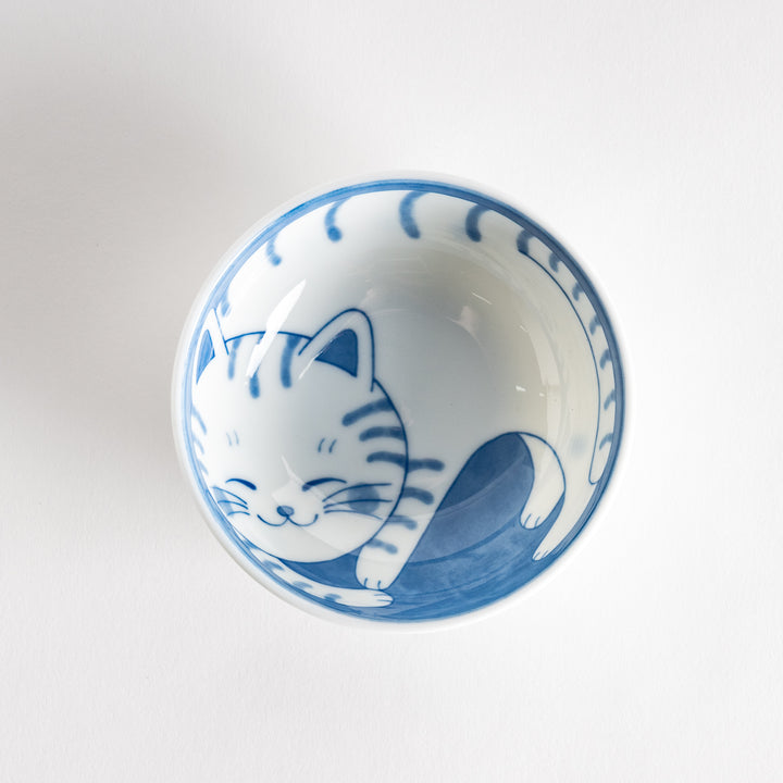 A dessert bowl with a blue-striped cat, smiling contentedly.