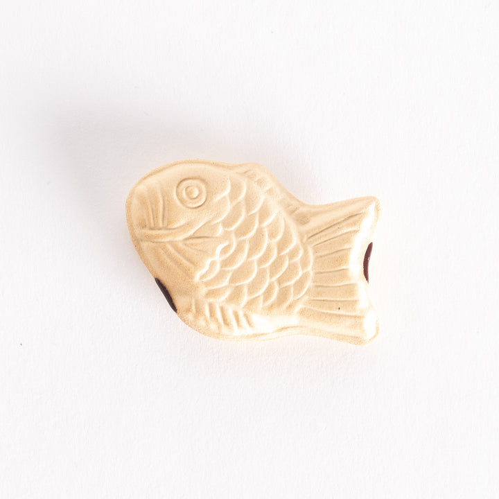 A ceramic chopsticks rest shaped like a taiyaki fish, featuring detailed scales and fins in a soft beige color.