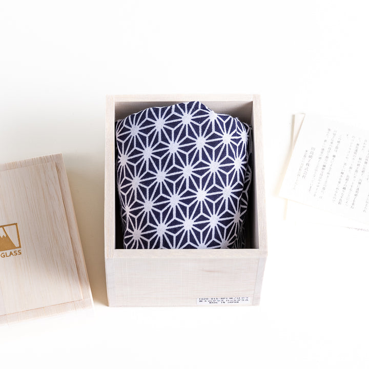 A blue and white geometric-patterned cloth is neatly folded inside a wooden box, with a label and a booklet beside it.