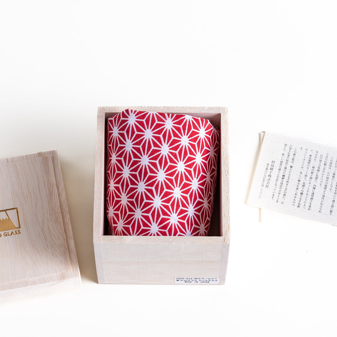 A red cloth with a white geometric-pattern, neatly folded inside a wooden box, accompanied by a small card with information.