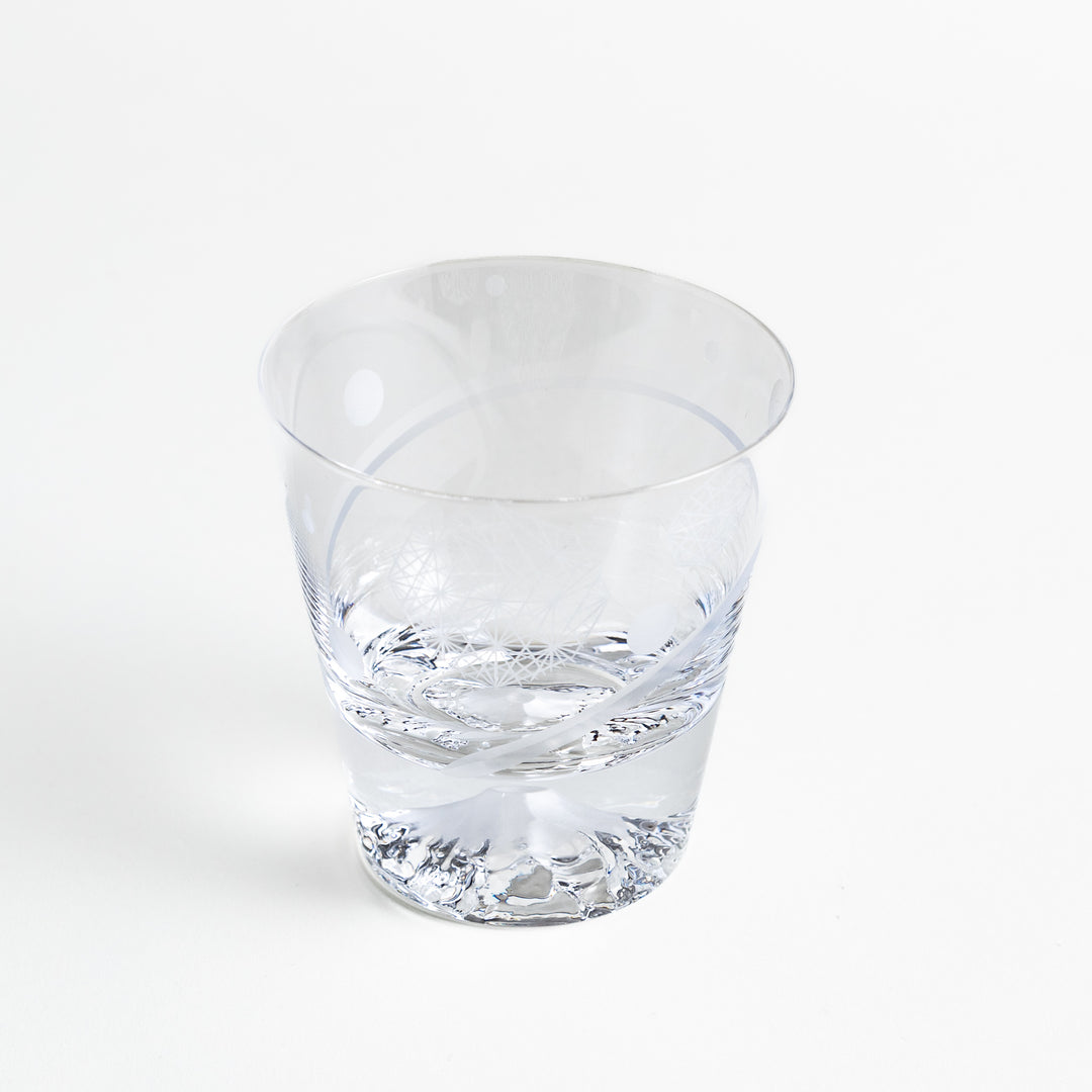 A clear glass with intricate patterns etched in geometric shapes and the bottom showing a mountain design.