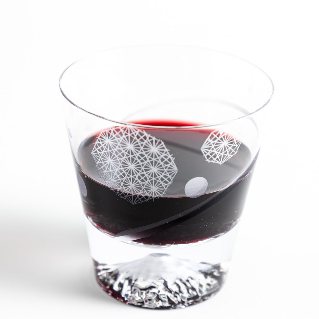 A close-up of a rocks glass filled with red wine, showing the geometric design.