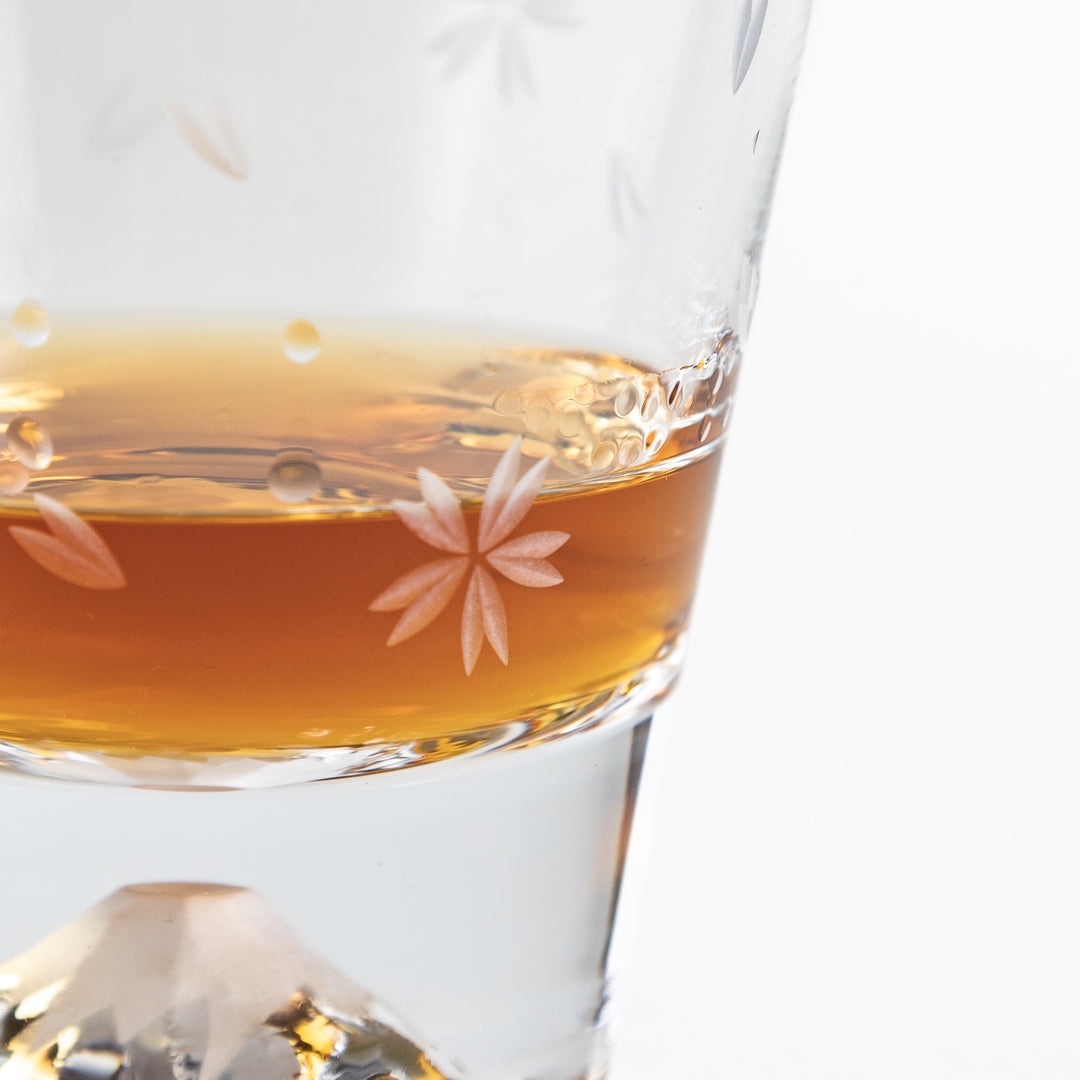 A glass filled with whisky featuring delicate sakura flower designs and the distinctive Mt. Fuji motif at the base.