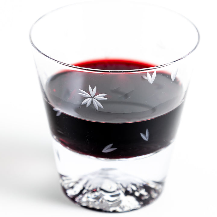 Close-up of a sakura-themed rocks glass filled with red wine, showing the sakura engraving and the mountain design at the bottom.