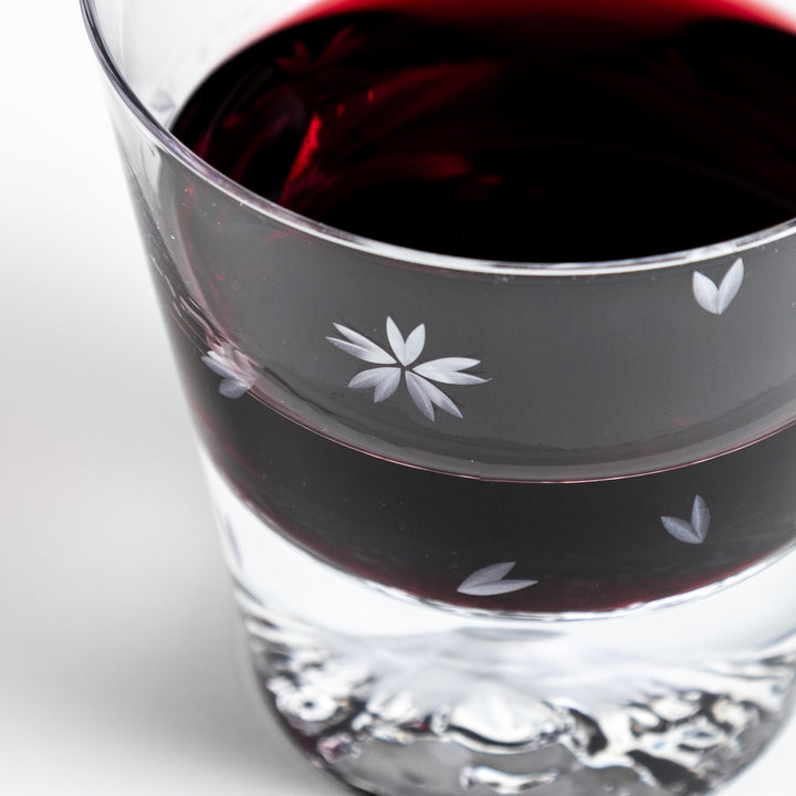 Close-up of a sakura-themed rocks glass filled with red wine, with clear visibility of the sakura flower engravings and the mountain base.