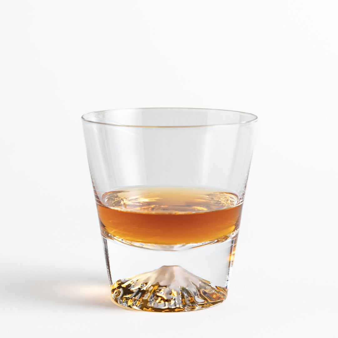 Glass with a whisky, showcasing an embossed Mount Fuji at the base, creating a striking visual effect.