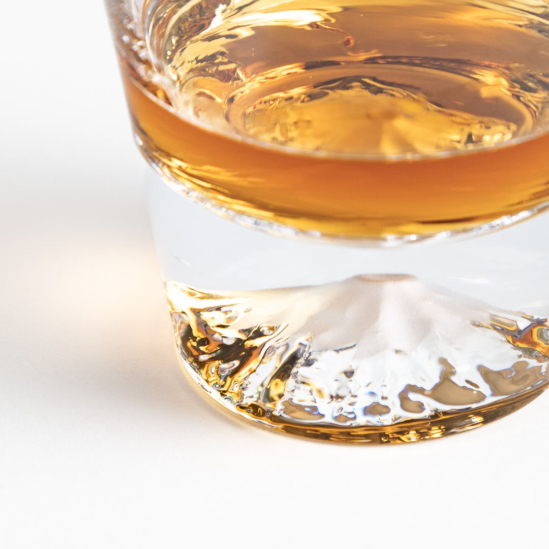 A close-up of the mountain-shaped base of a glass filled with Whisky, showing the detail of the glass design.