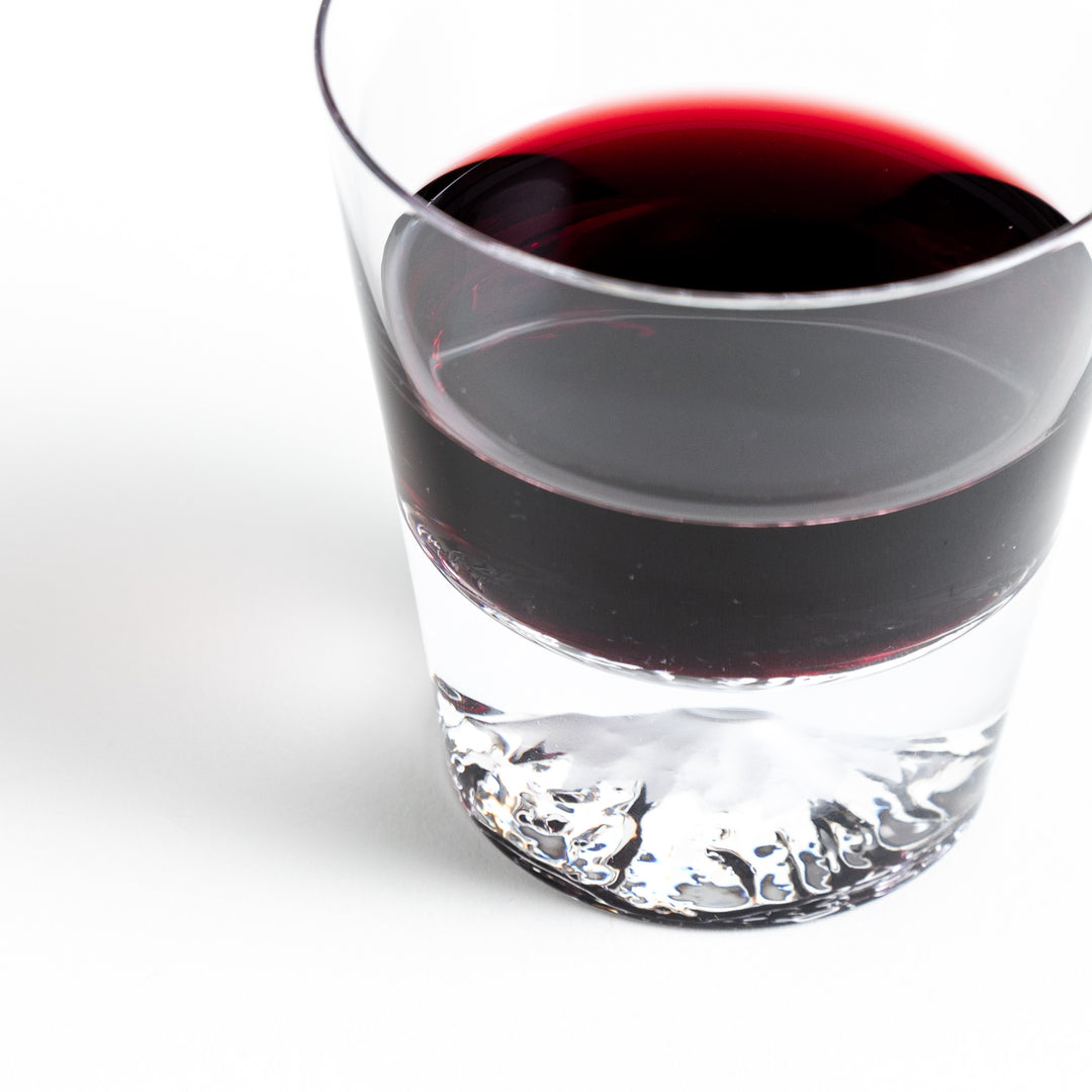 Close-up of a glass with red wine, showcasing intricate details of the embedded Mount Fuji design at the bottom.