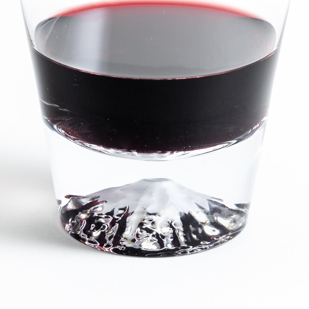 A close-up shot of a whisky glass filled with red wine, showing the distinct mountain design at the base of the glass."