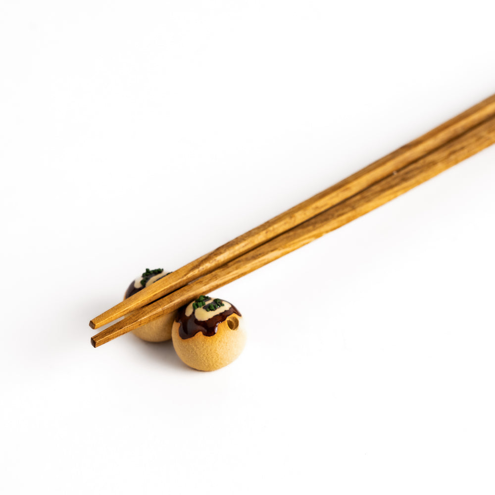 Wooden chopsticks resting on a pair of takoyaki-shaped chopstick rests, a fun and functional addition to any Japanese dining setting.