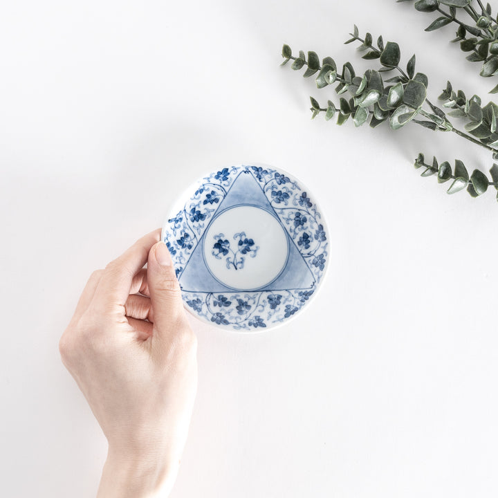 Hand holding the three-sided sauce dish from above, displaying the intricate blue floral arabesque pattern and central circle.