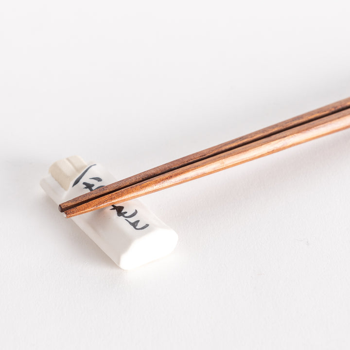 Close-up of white ceramic chopsticks rest with chopsticks placed, highlighting the bag-like design.