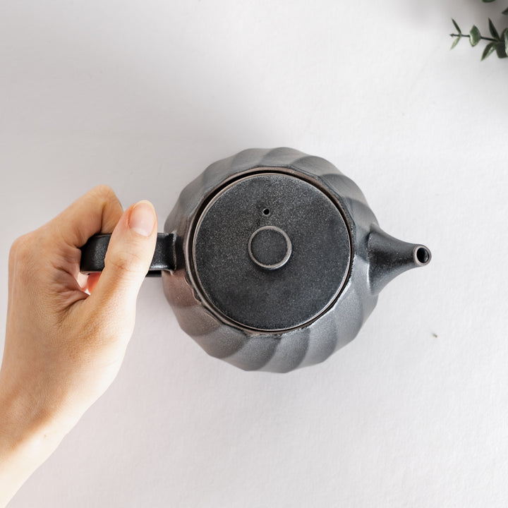 Hand holding the black teapot from above, showcasing its stylish design and smooth finish.