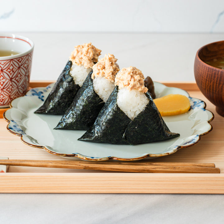 Top view of tuna mayo onigiri (rice balls) wrapped in nori, served with a cup of tea, pickled vegetables, and a bowl of miso soup.