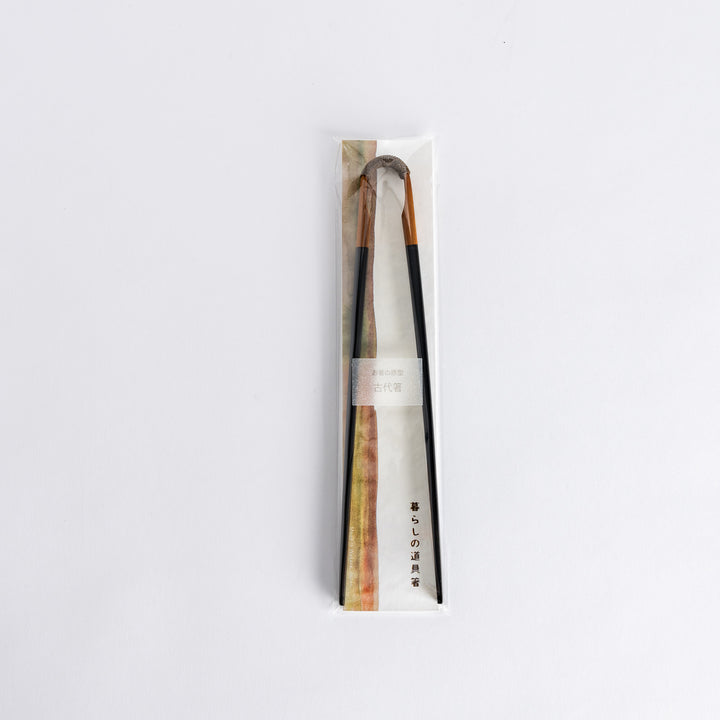 Vintage chopsticks with a wooden handle and black lacquered tips, packaged in a simple paper wrapper.