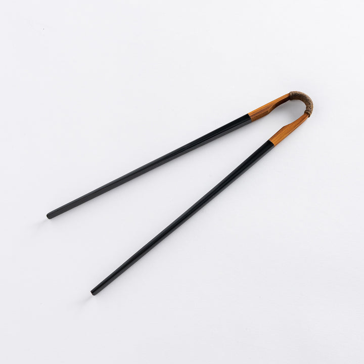 Black lacquered chopsticks with a curved wooden handle wrapped in twine, close-up of the tip.