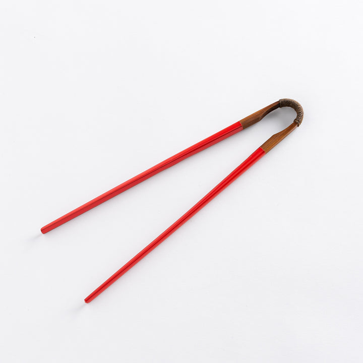 Red chopsticks with a winding at the top and a wooden base, laid flat.