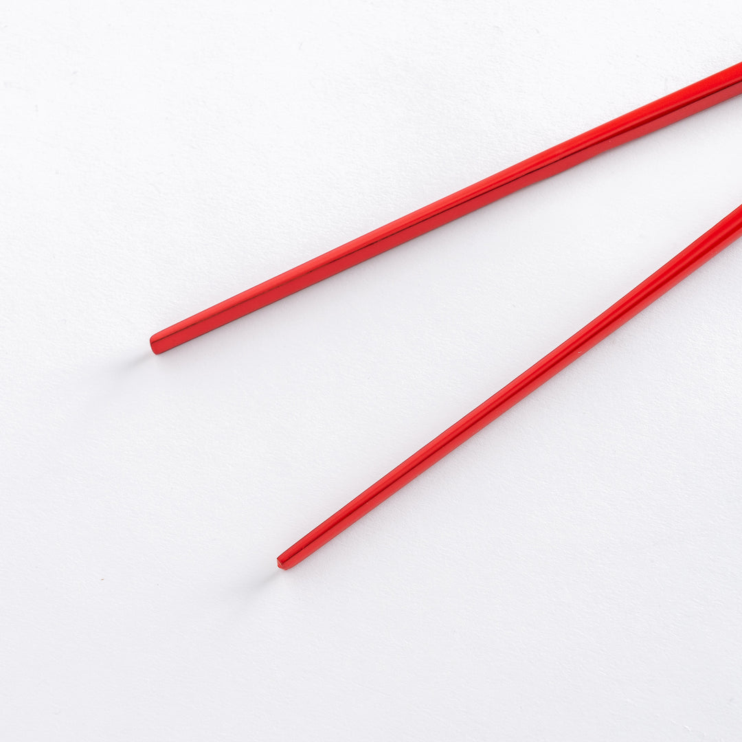 Close-up of red chopsticks, displaying their smooth finish with square edges and a shiny, polished appearance.