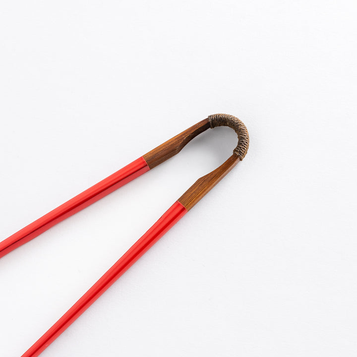 Close-up of the curved wooden joint of red chopsticks, showing the natural wood and elegant craftsmanship that connects the chopsticks.